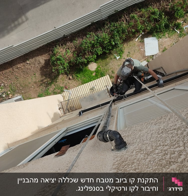 אדם עם ציוד טיפוס ליד צינור על קיר חיצוני